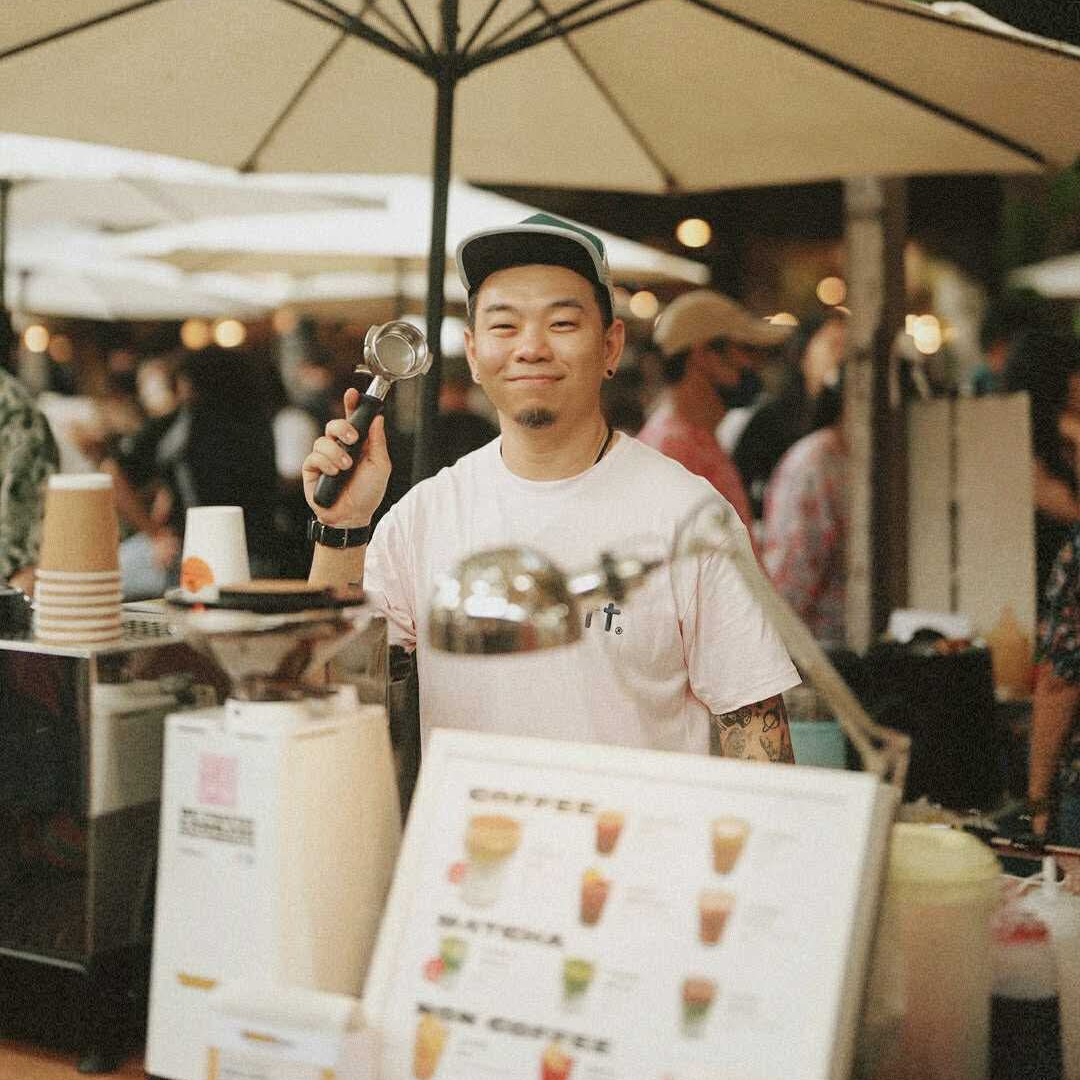 Man holding a coffee-making device at an outdoor market stall.